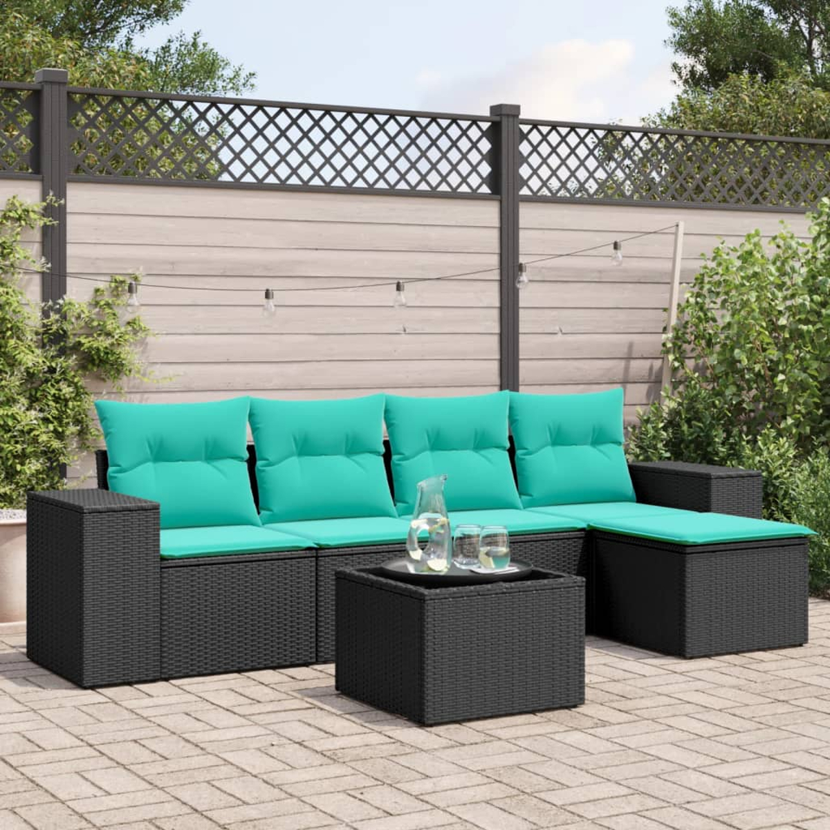 Gartensektionssofa mit türkisfarbenen Kissen und einem passenden Couchtisch. Dahinter ein Holzzaun und Lichterketten.