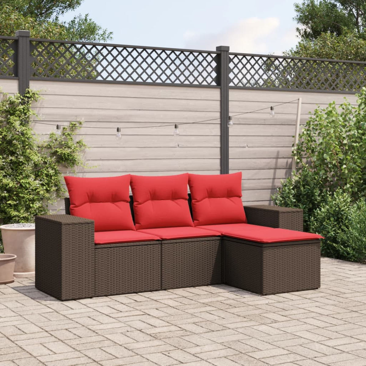 Braunes Korbmöbel-Ecksofa mit roten Kissen steht auf einer Terrasse. Im Hintergrund sind ein Holzzaun und Pflanzen.