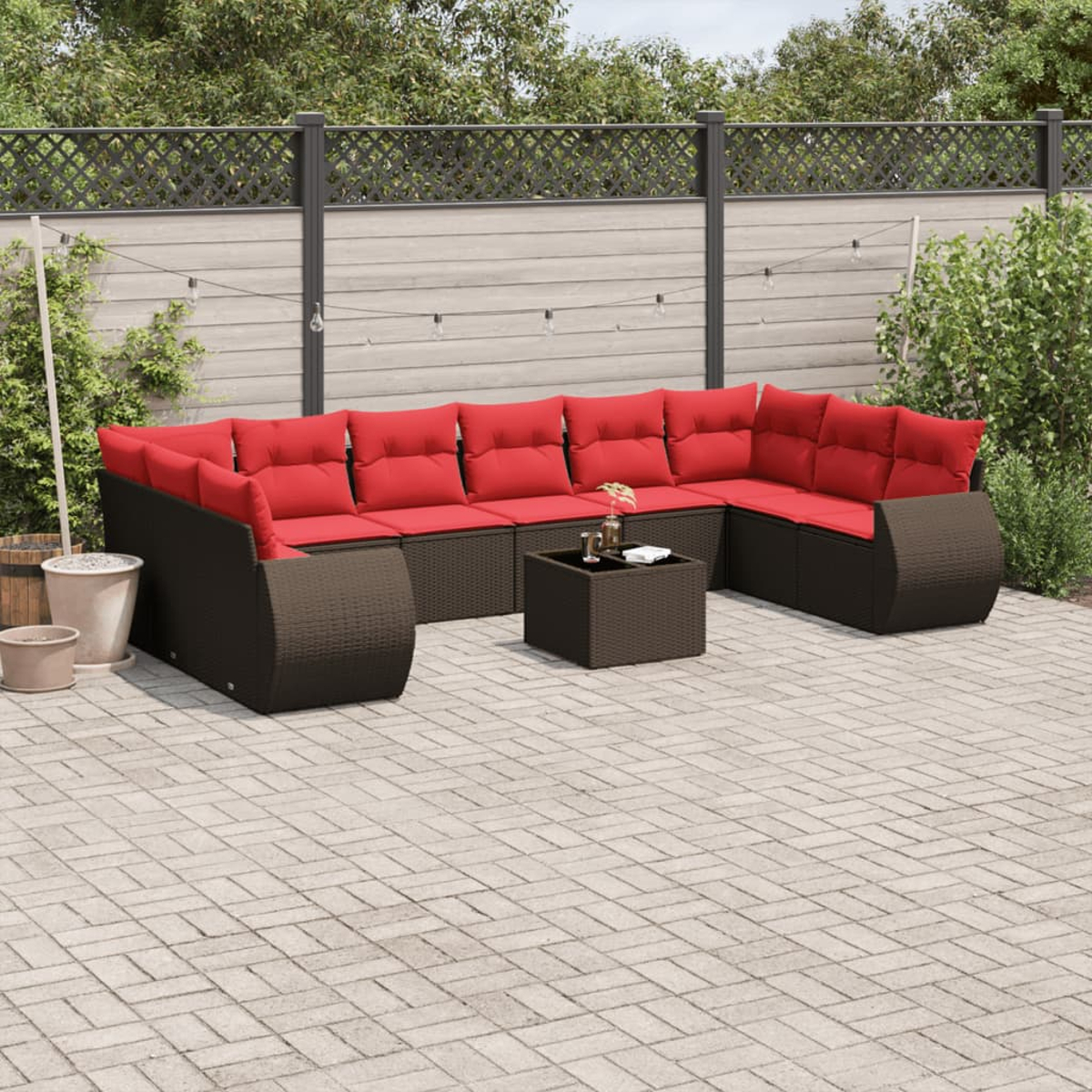 Ein Ecksofa mit roten Kissen im Freien steht auf einer Terrasse. Ein kleiner Tisch mit Getränken steht davor. Hinten ist ein Holzzaun.