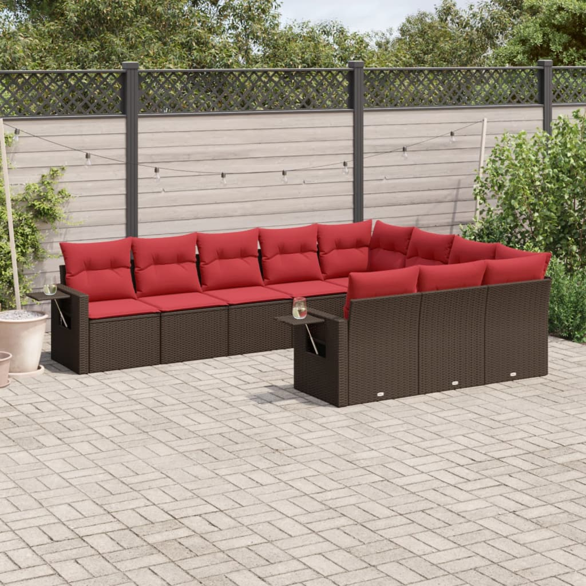 Outdoor-Ecksofa mit roten Kissen auf einer Backstein-Terrasse, umgeben von Grün und einem Holzzaun.