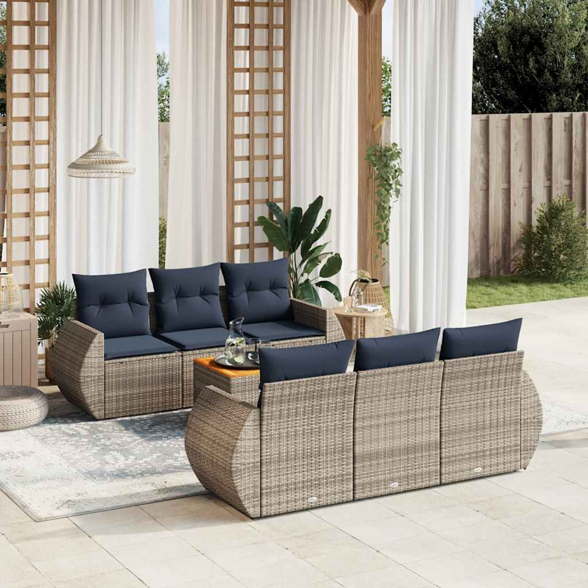 Outdoor-Sitzgruppe mit marineblauen Kissen. Ein gewebtes, graues Sofa steht einem passenden Loveseat gegenüber, mit einem Couchtisch. Durchsichtige Vorhänge im Hintergrund.