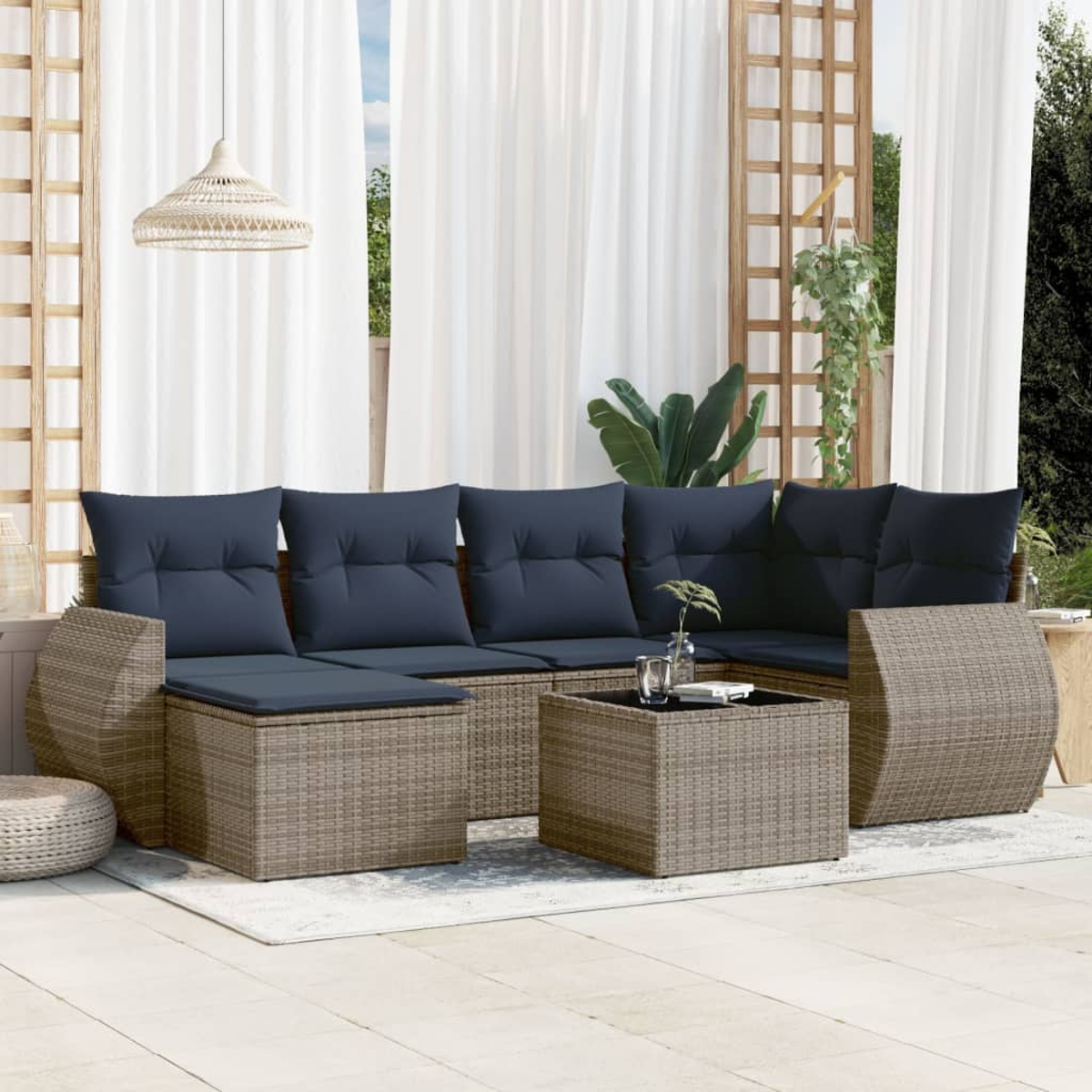 Rattan-Sofa im Freien mit marineblauen Kissen, einem Couchtisch und einem weißen Teppich auf einer Terrasse. Weiße Vorhänge im Hintergrund.