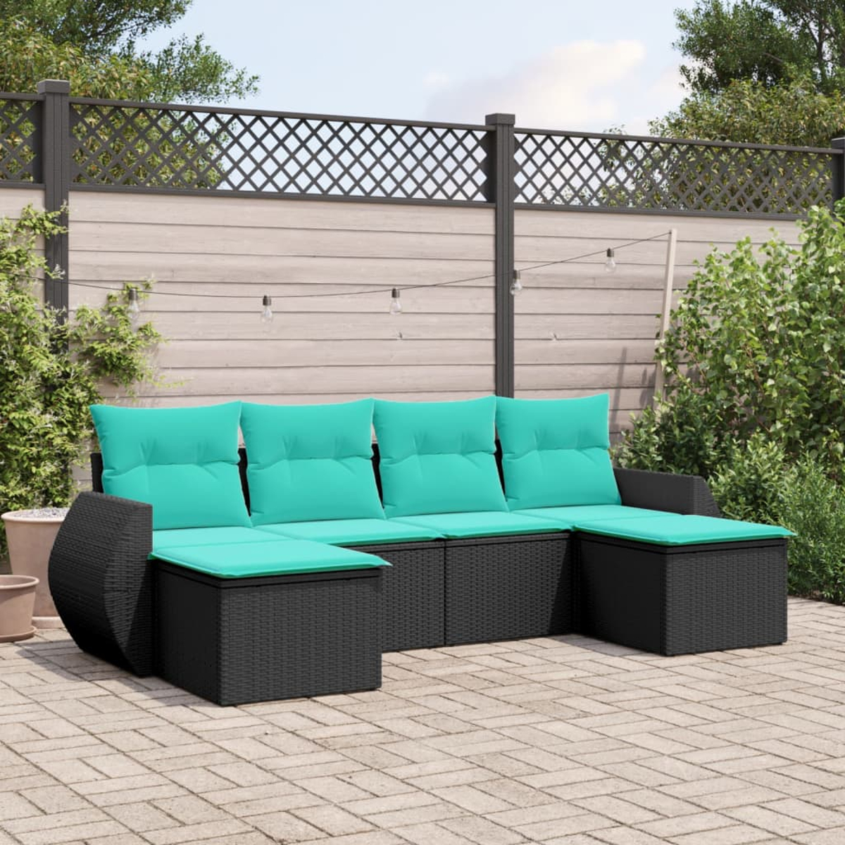 Ein schwarzes Outdoor-Ecksofa aus Korbgeflecht mit türkisfarbenen Kissen steht auf einer Backstein-Terrasse. Dahinter ein Holzzaun und Grün.