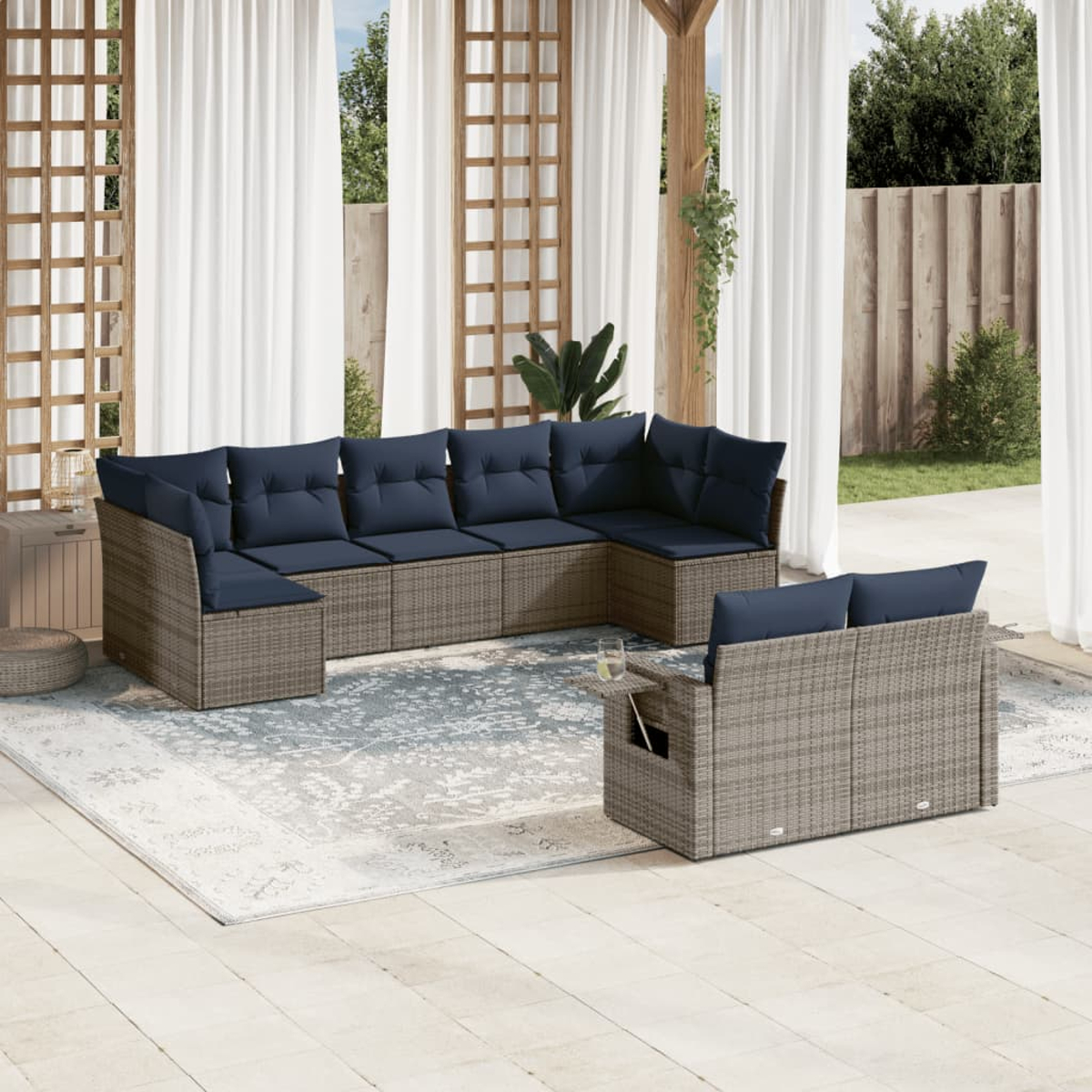 Outdoor-Ecksofa mit marineblauen Kissen auf einem gemusterten Teppich. Weiße Vorhänge und Holzgitter im Hintergrund. Ein Glas Wasser steht auf dem Beistelltisch.