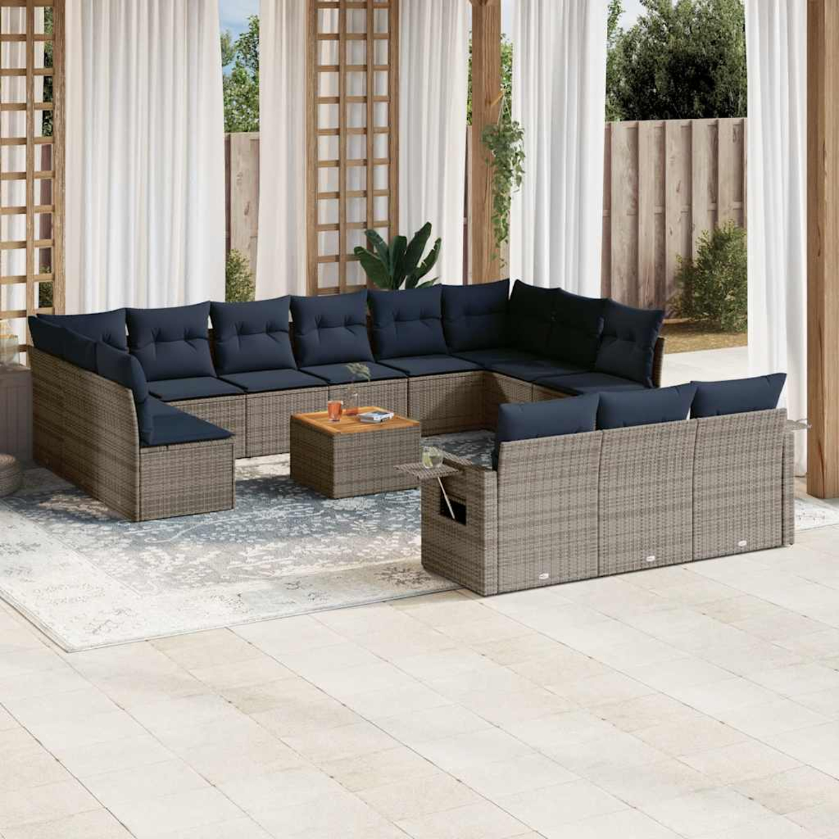 Un juego de patio con cojines azules está sobre una alfombra, una mesa pequeña con bebidas y cortinas blancas al fondo.