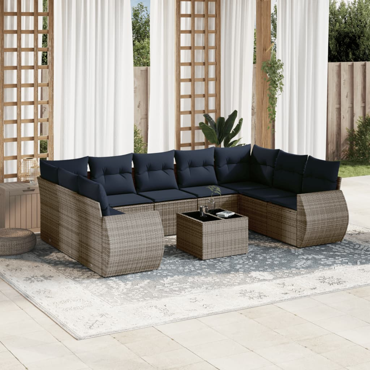 Outdoor-Sitzbereich. Korbmöbel mit marineblauen Kissen, Couchtisch, Teppich und transparenten Vorhängen. Hintergrund: Holzgitter und Zaun.