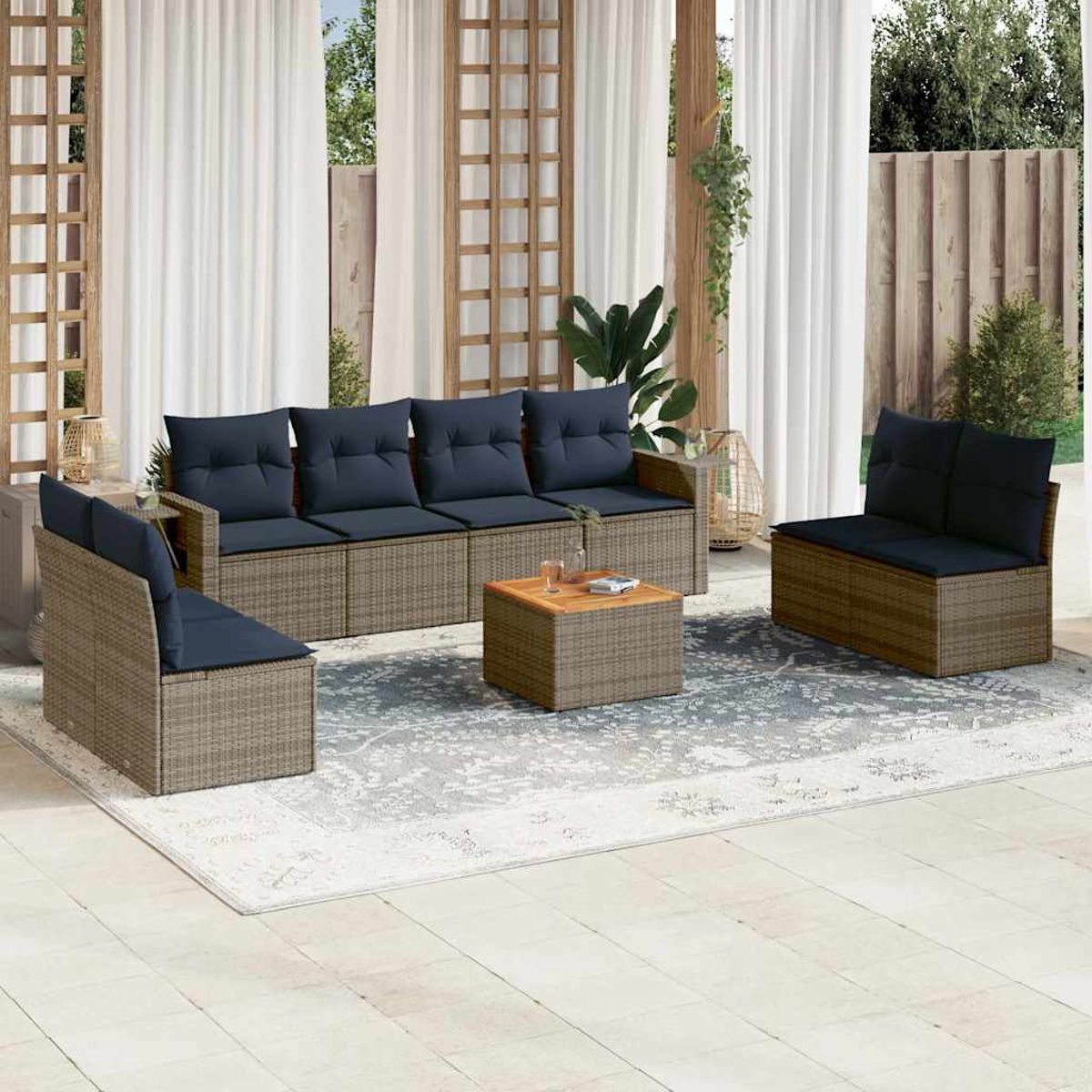 Terrassenset mit Sofa, zwei Stühlen und einem Couchtisch. Dunkelblaue Kissen auf Korbmöbeln. Weiße Vorhänge und Gartenhintergrund.