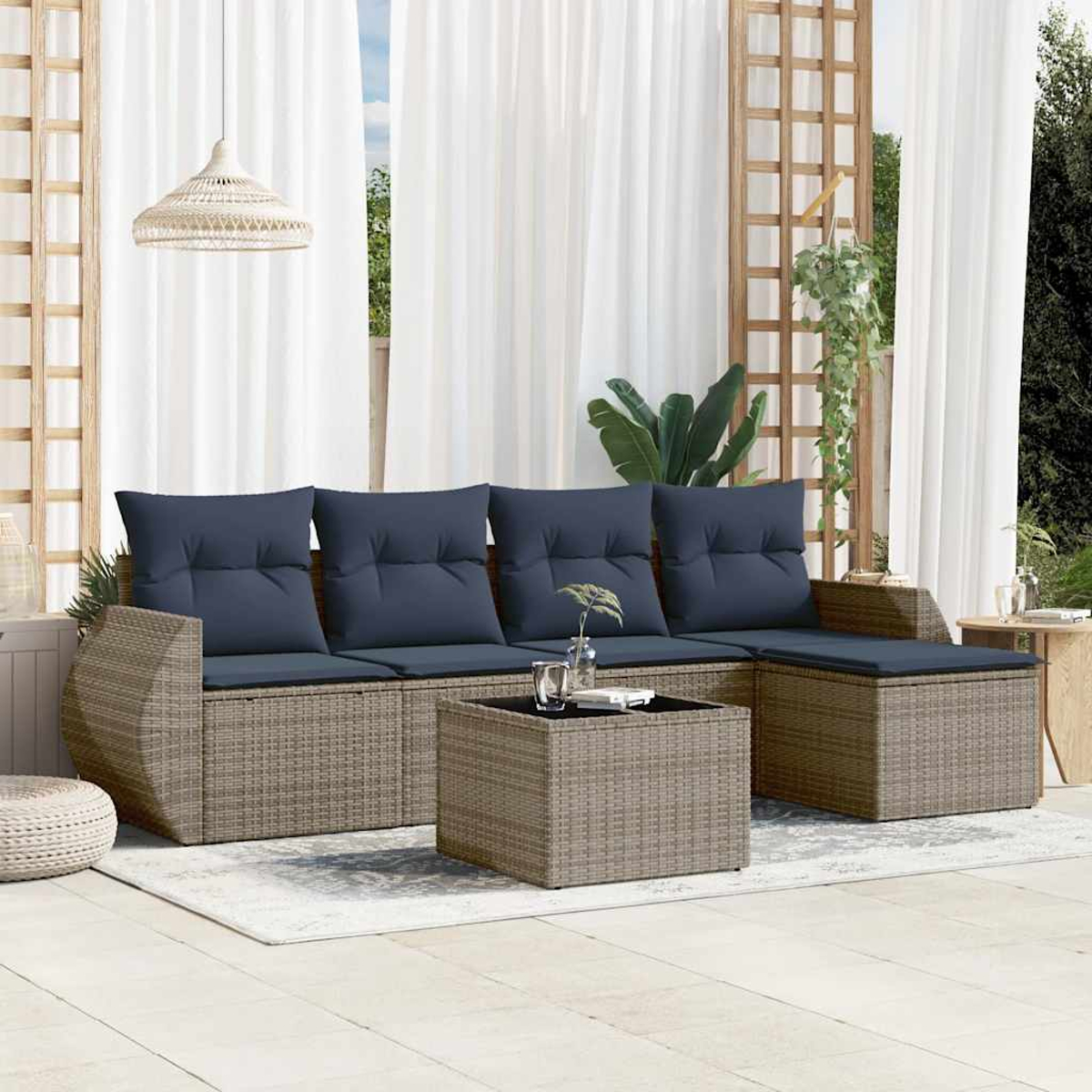 Outdoor-Sitzgruppe mit blauen Kissen, Weidenrahmen, Couchtisch und Ottomane. Der Hintergrund umfasst Vorhänge und Grün.
