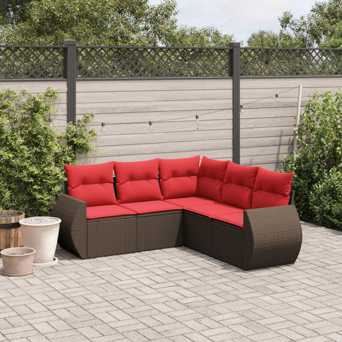 Sofá seccional al aire libre con cojines rojos en un patio de ladrillos. Una valla de madera y plantas al fondo.
