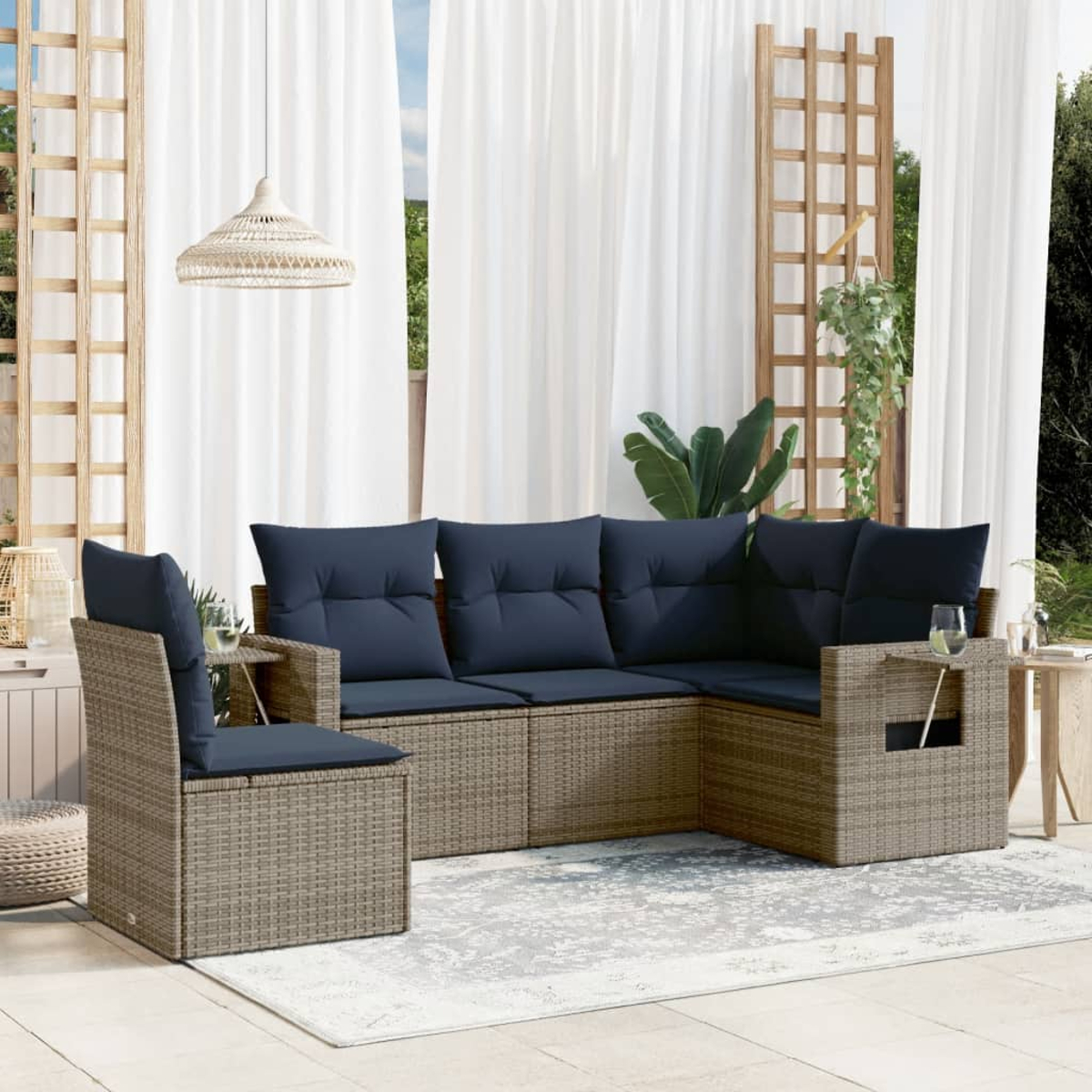 Outdoor-Sitzbereich mit Korbmöbeln. Ein Ecksofa und ein Stuhl mit marineblauen Kissen stehen auf einem Teppich vor weißen Vorhängen.