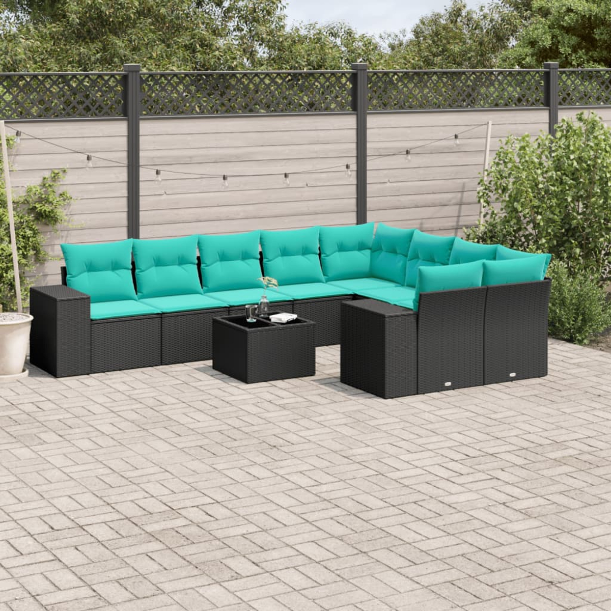 Sofá seccional al aire libre con cojines turquesa y una mesa negra. Está sobre un patio de ladrillos, con una valla y vegetación de fondo.