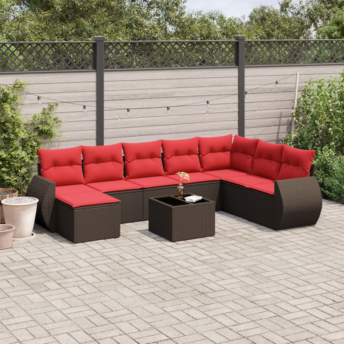 Outdoor-Ecksofa mit roten Kissen auf einer Terrasse. Braune Korbmöbel, Couchtisch, Lichterkette und Zaun sind sichtbar.