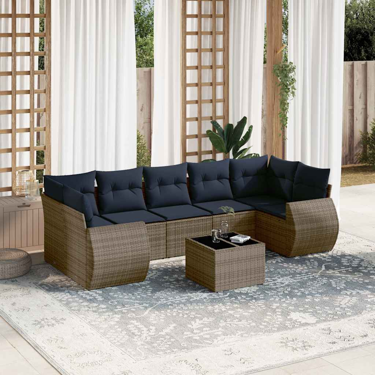 Outdoor-Ecksofa mit marinefarbenen Kissen, Korbgewebe und passendem Couchtisch auf einem gemusterten Teppich, in der Nähe weißer Vorhänge.