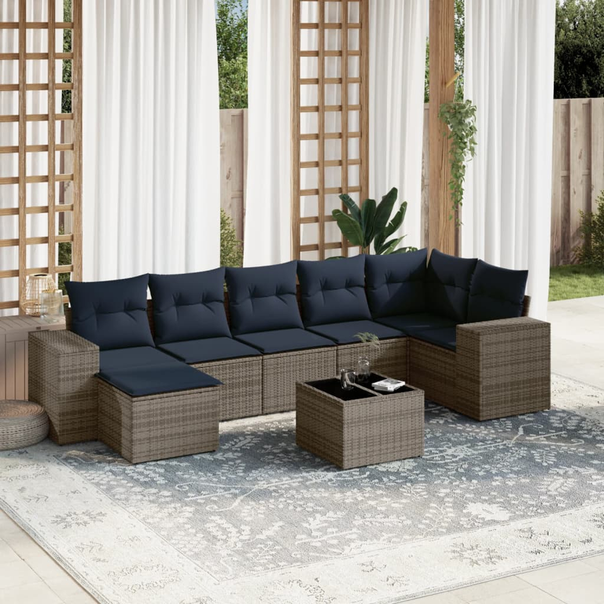 Outdoor-Ecksofa mit marineblauen Kissen auf einem gemusterten Teppich. Weiße Vorhänge und Holzgitter im Hintergrund. Ein kleiner Couchtisch.
