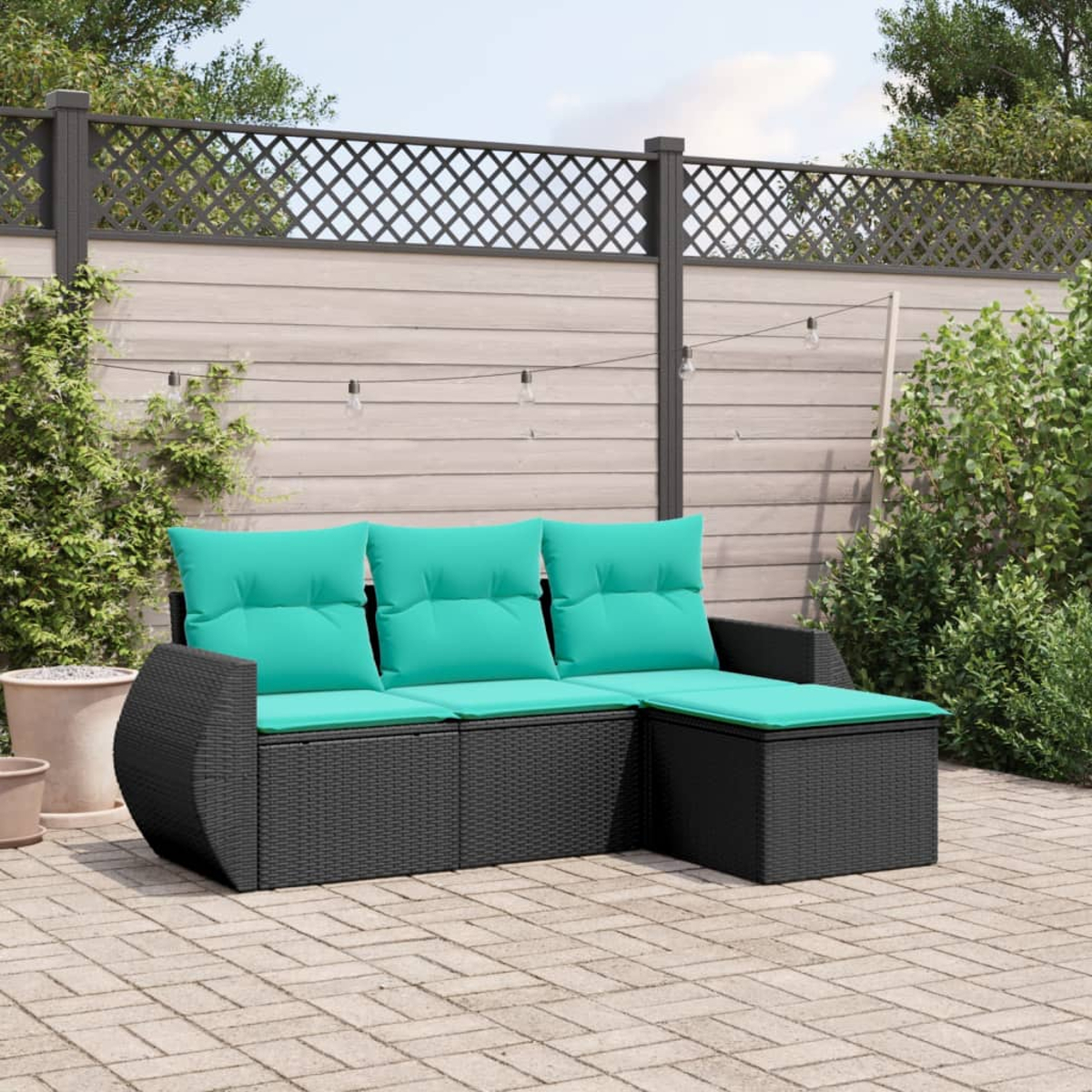 Schwarzes Outdoor-Sofa aus Korbgeflecht mit türkisfarbenen Kissen auf einer Ziegelterrasse. Hintergrund: Zaun, Pflanzen und Lichterketten.