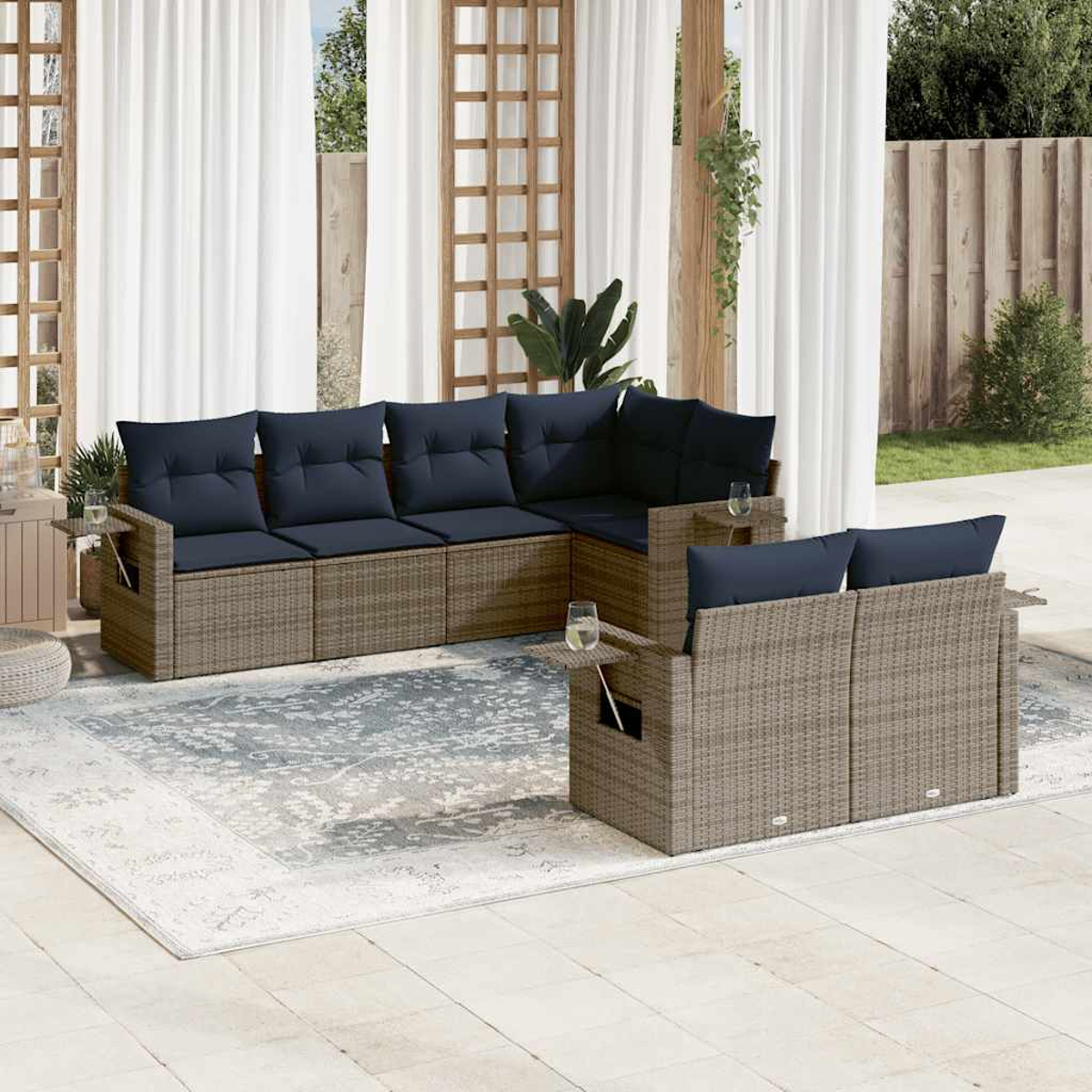 Garten-Terrassenset mit blauen Kissen. Beige Korbmöbel auf einem gemusterten Teppich. Weiße Vorhänge und Holzgitter im Hintergrund.