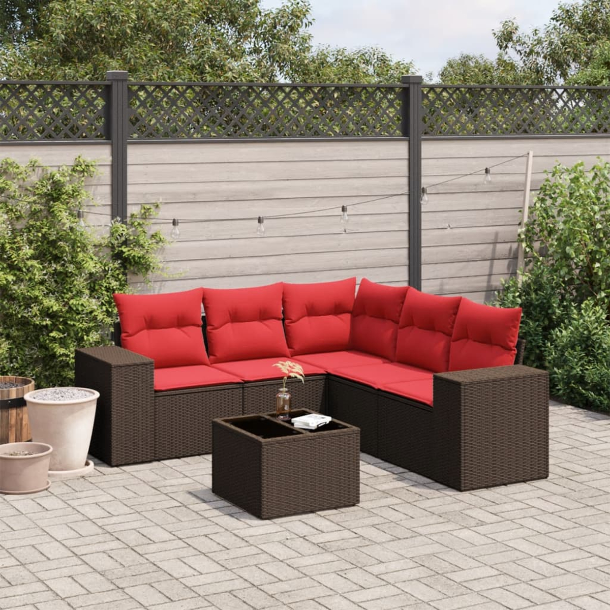 Gartensofa mit roten Kissen und passendem Couchtisch auf einer Ziegelterrasse. Zaun und Pflanzen im Hintergrund.