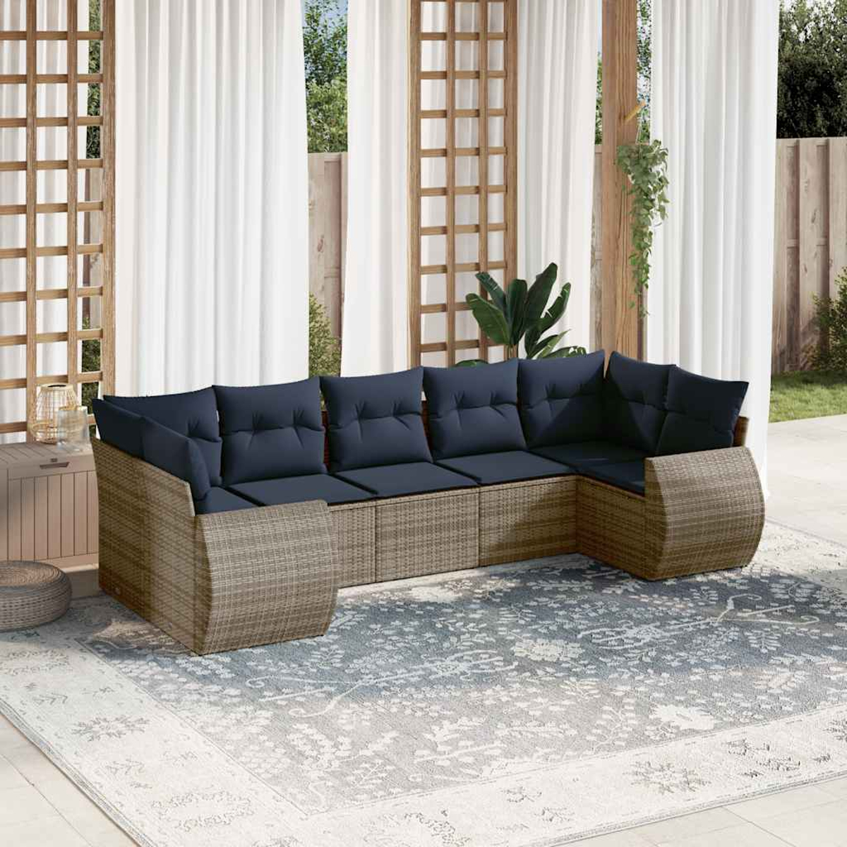 Outdoor-Ecksofa mit blauen Kissen auf einem gemusterten Teppich. Weiße Vorhänge und Holzgitter im Hintergrund. Pflanzen sind sichtbar.