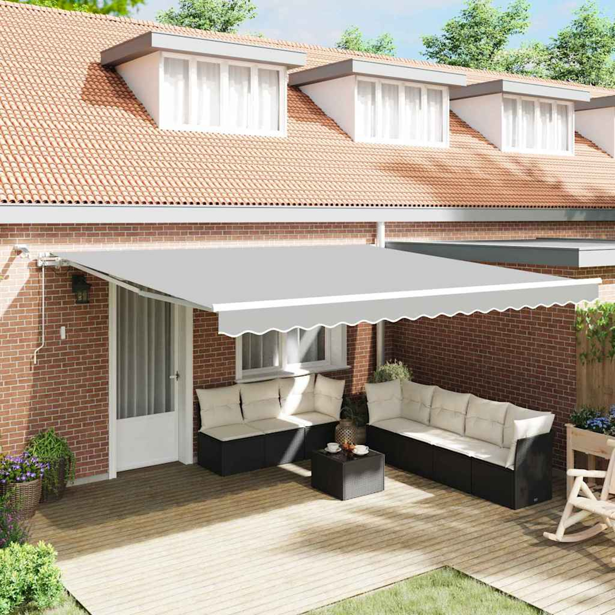 Eine Terrasse mit grauem Vordach, Sofas und einem Couchtisch. Rote Backsteinmauer, Holzterrasse und ein Haus mit Dachgauben im Hintergrund.