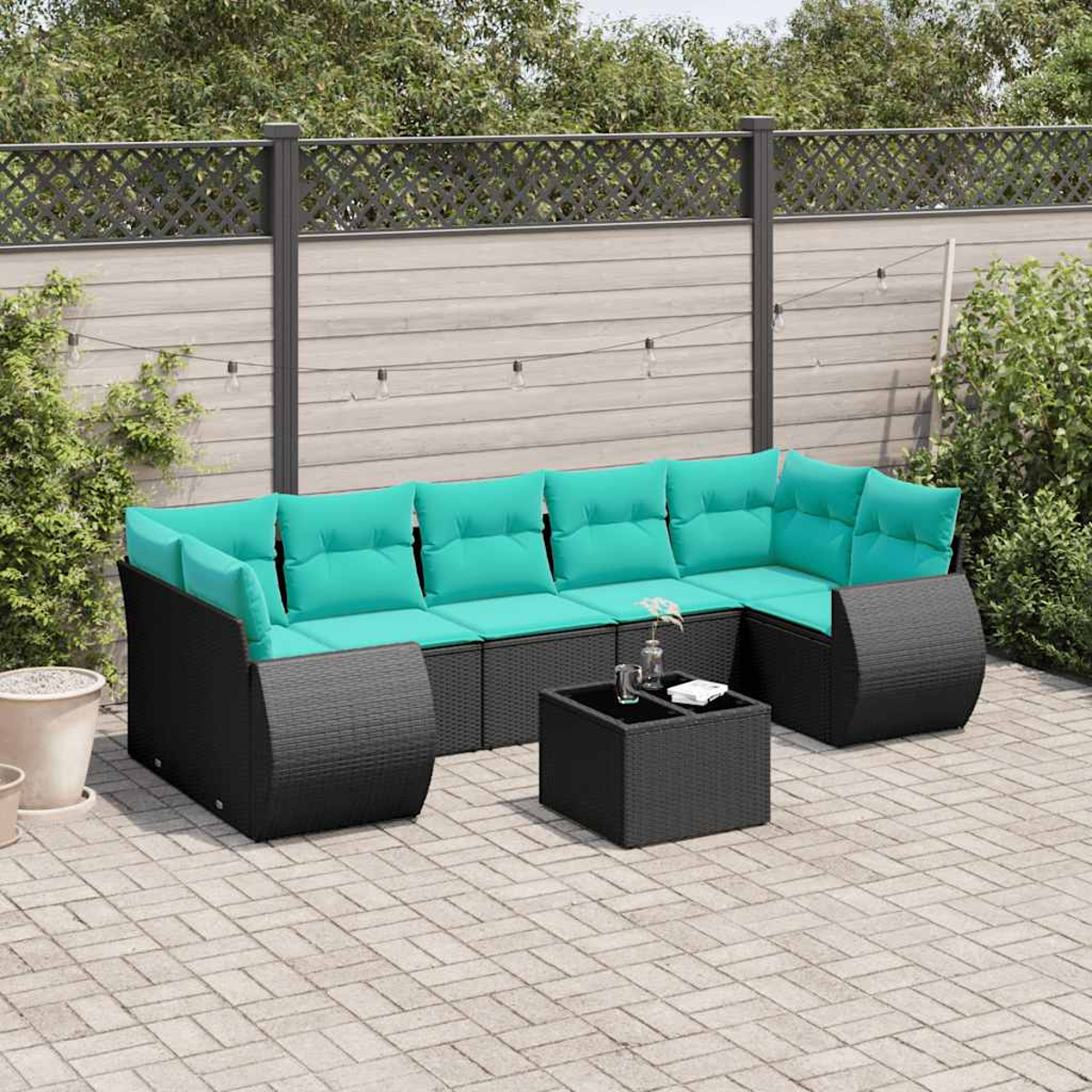 Juego de asientos al aire libre con cojines turquesa y mimbre negro. Incluye una mesa de centro en un patio pavimentado. Fondo con valla y plantas.