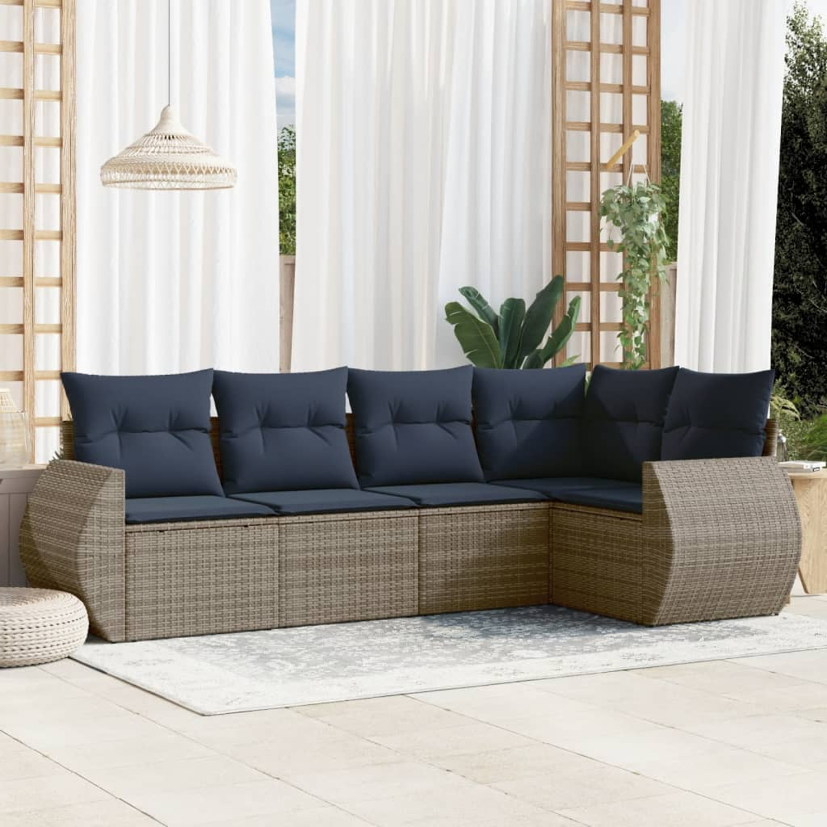 Ein Ecksofa mit blauen Kissen steht auf einer Terrasse. Weiße Vorhänge und ein Holzgitter im Hintergrund.