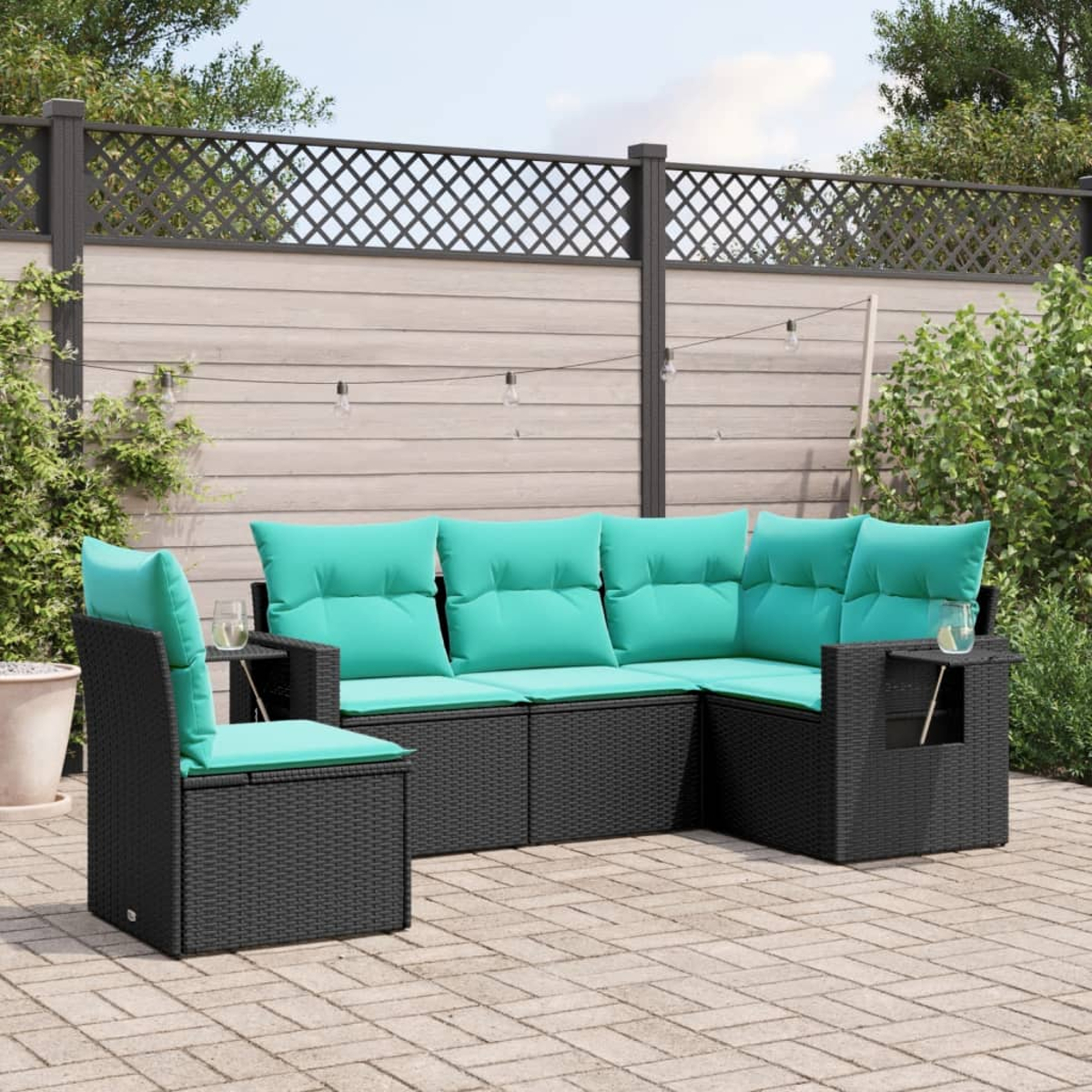 Schwarzes Outdoor-Geflecht-Sofa mit teal-farbenen Kissen auf einer Ziegelterrasse. Ein Zaun und Grünzeug sind im Hintergrund.