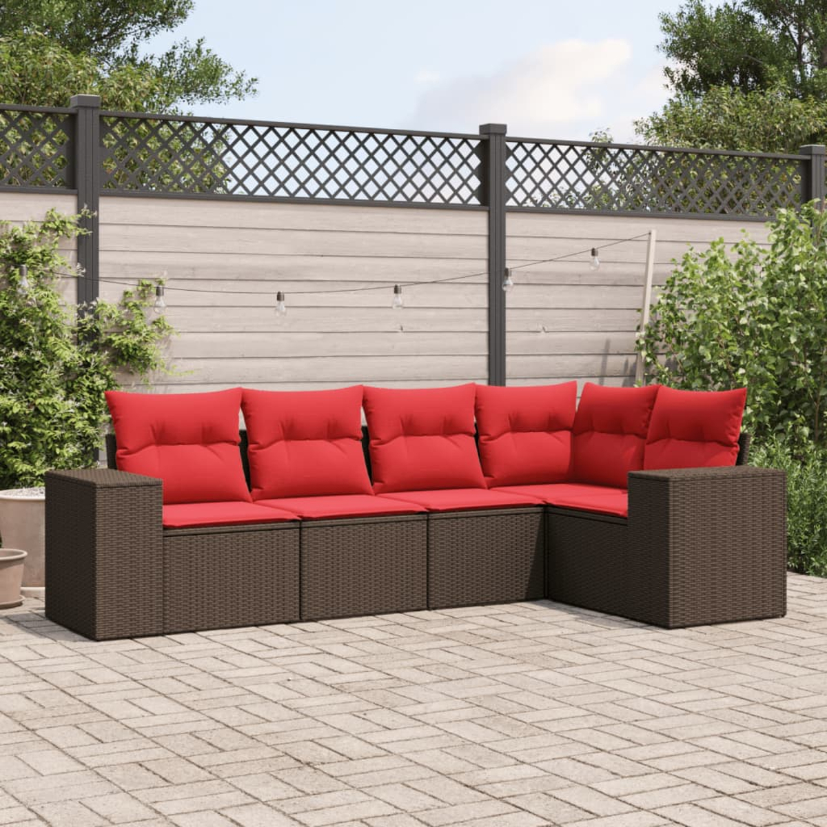 Ein Ecksofa im Freien mit roten Kissen. Es ist braun und steht auf einer Ziegelterrasse. Im Hintergrund befinden sich ein Zaun und Grün.
