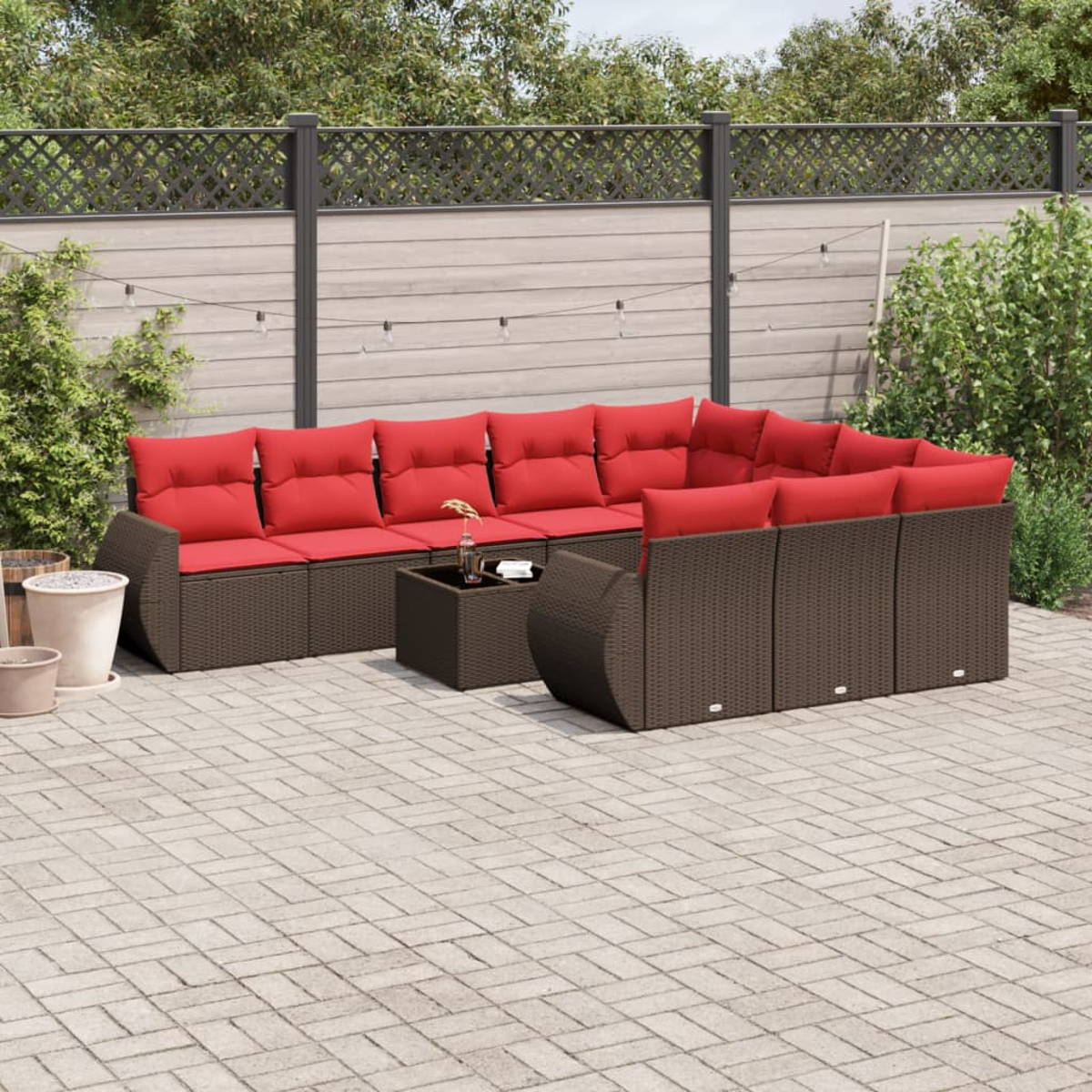 Garten-Set mit braunem Korbgewebe und roten Kissen. Beinhaltet ein Ecksofa, einen Couchtisch und eine Backstein-Terrasse.