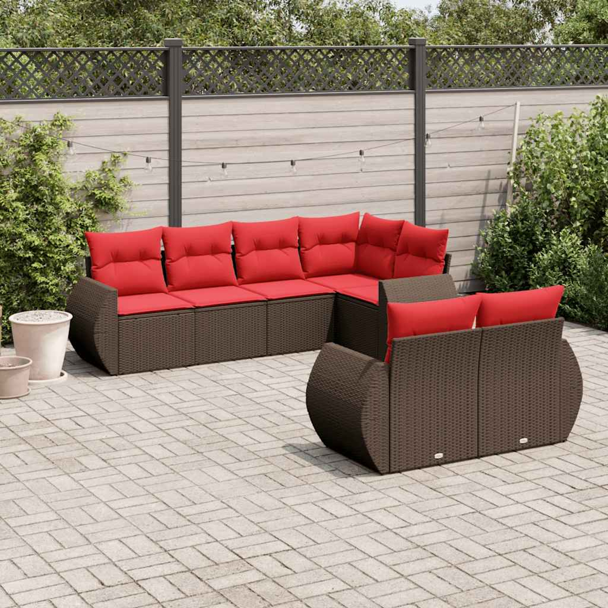 Szene im Freien mit braunen Korbsesseln und roten Kissen. Im Vordergrund befindet sich eine Terrasse und im Hintergrund ein Holzzaun.