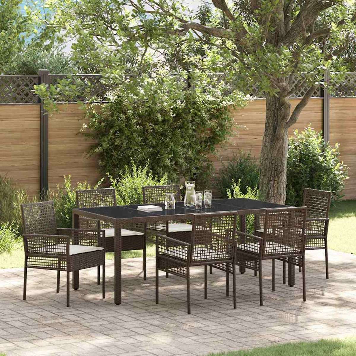 Ein brauner Korbtisch und Stühle auf einer Terrasse. Auf dem Tisch stehen ein klarer Krug und Gläser. Bäume und ein Zaun sind im Hintergrund.