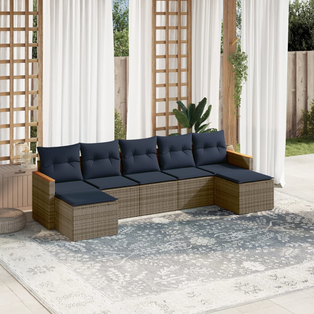 Ein Sitzbereich im Freien mit einem Ecksofa mit blauen Kissen auf einem gemusterten Teppich, weißen Vorhängen und Holzakzenten.