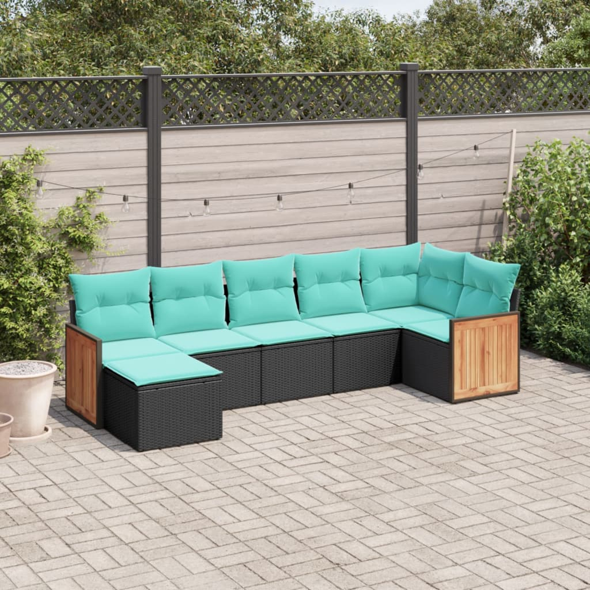 Ein Terrassenset mit türkisfarbenen Kissen auf einer Ziegelterrasse. Der Hintergrund umfasst einen Zaun und Grün.