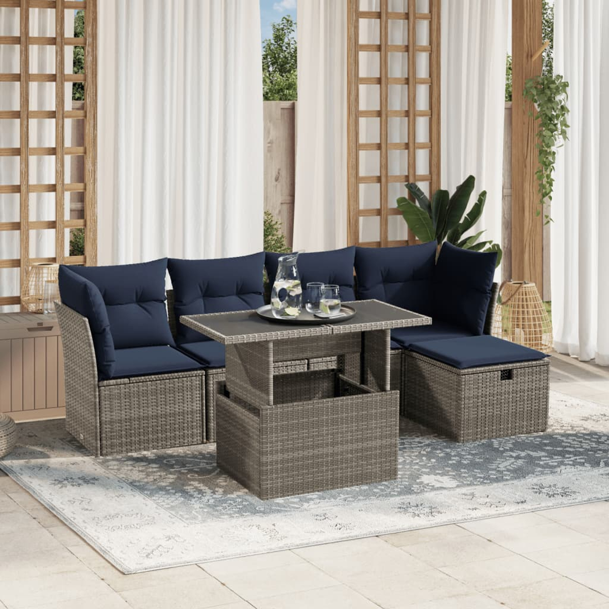 Garten-Sitzgruppe mit marineblauen Kissen und einem Tisch mit Hubfunktion. Auf dem Tisch stehen ein Krug und Gläser. Vorhänge und Grün im Hintergrund.
