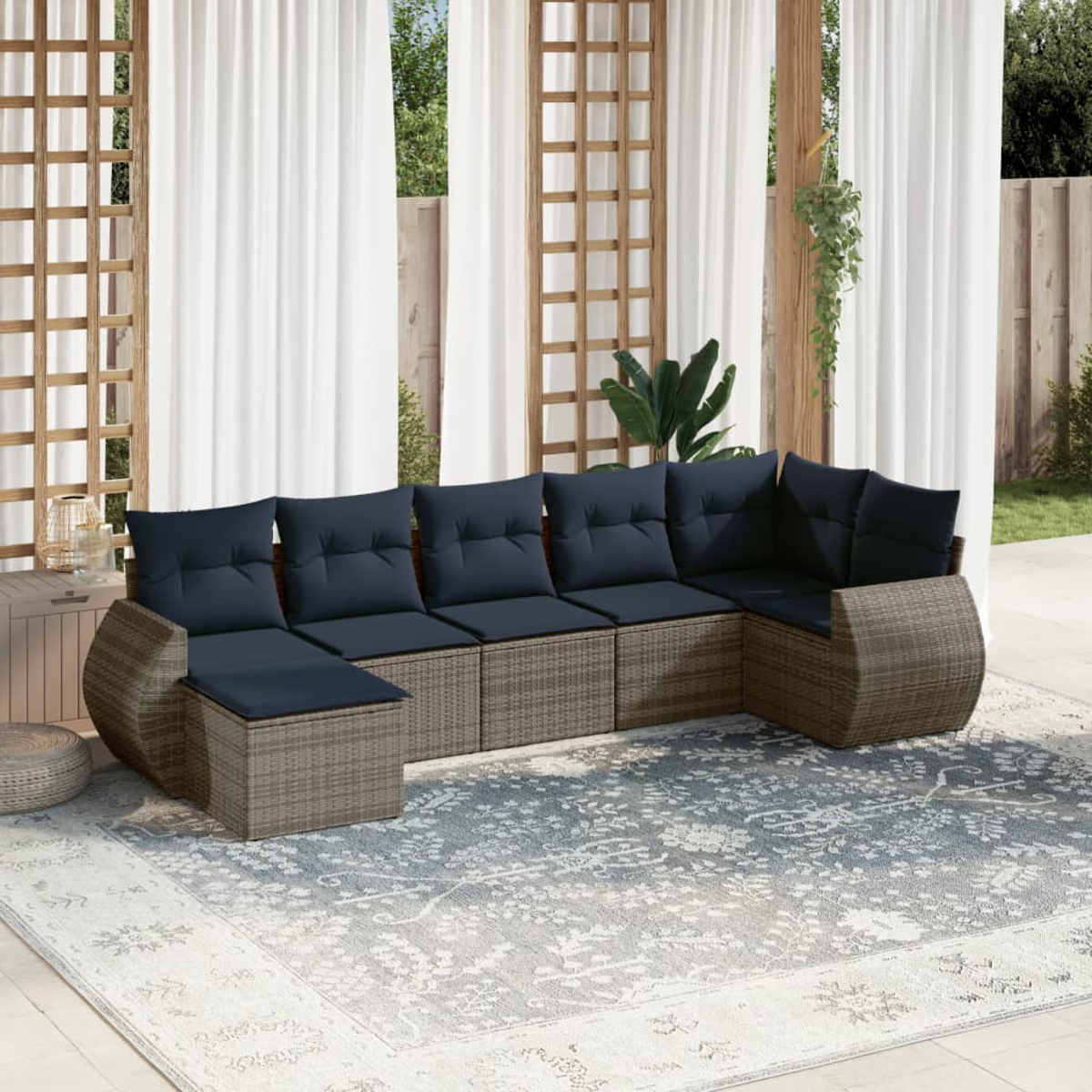 Ein Sitzbereich im Freien mit einem großen Ecksofa mit marineblauen Kissen, einem gemusterten Teppich und durchsichtigen weißen Vorhängen.