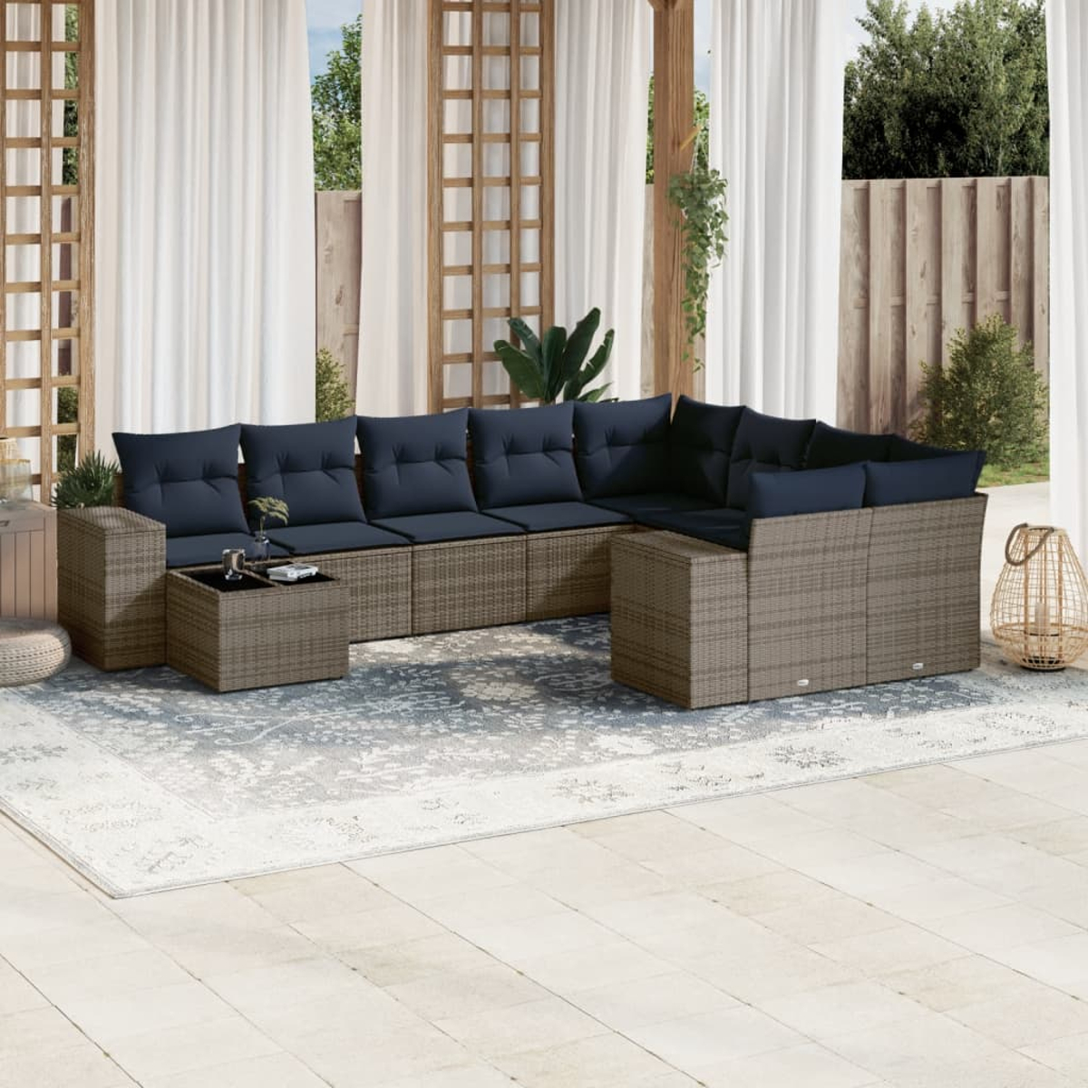 Outdoor-Ecksofa mit marineblauen Kissen, Couchtisch, Teppich und Vorhängen. Im Hintergrund sind Bäume und ein Holzgitter.