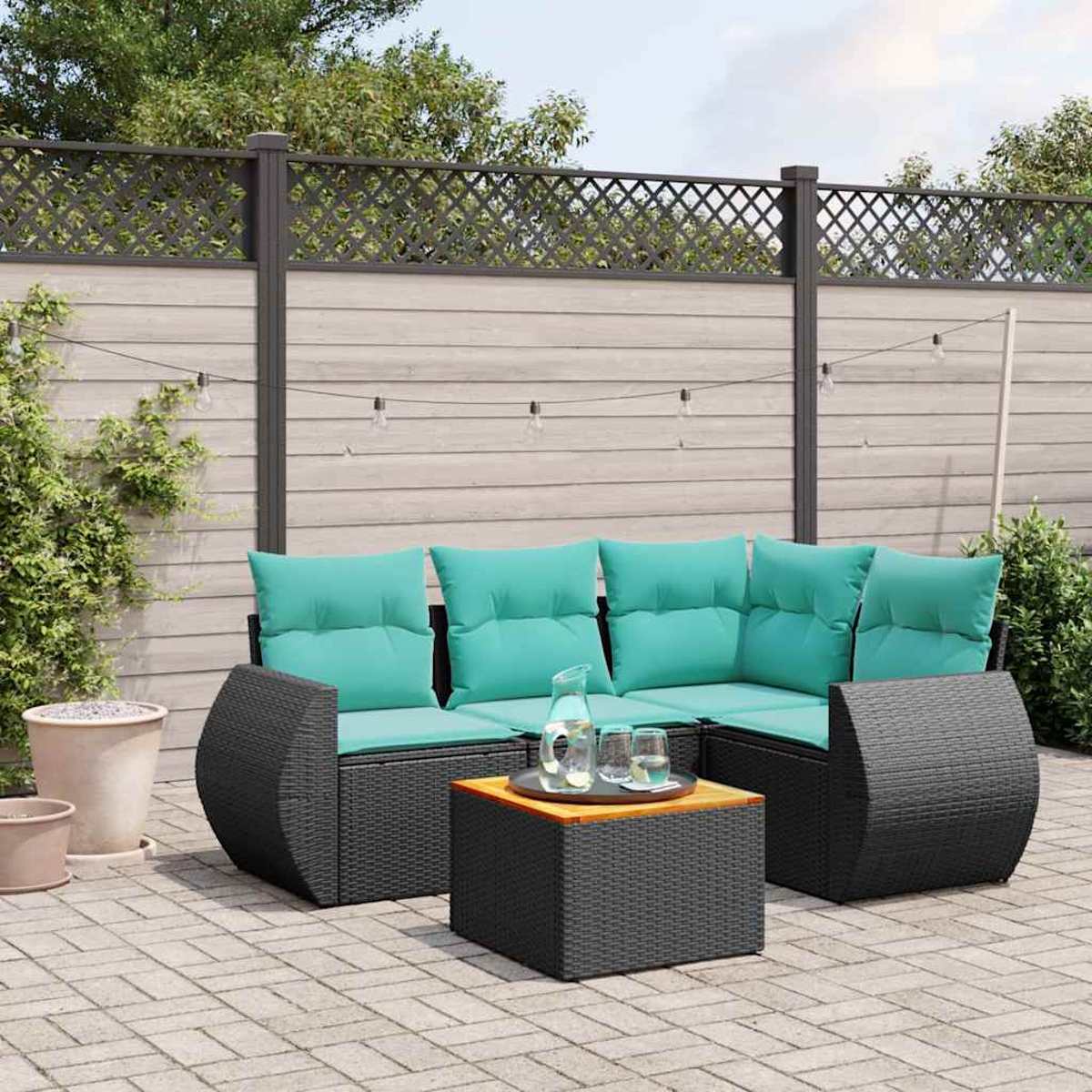 Garten-Sitzgruppe mit türkisfarbenen Kissen, einem schwarzen gewebten Tisch und einem Holzzaun im Hintergrund. Klare Gläser auf dem Tisch.