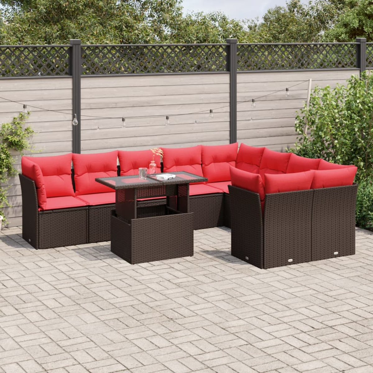 Garten-Set mit roten Kissen. Braune Korbmöbel umfassen Ecksofa und Couchtisch auf einer gepflasterten Terrasse.