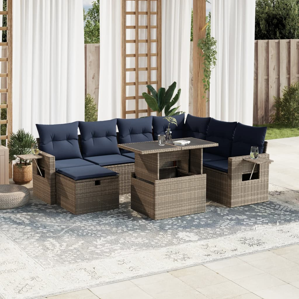 Garten-Set mit blauen Kissen, einem Tisch mit Getränken, auf einem gemusterten Teppich und weißen Vorhängen im Hintergrund.
