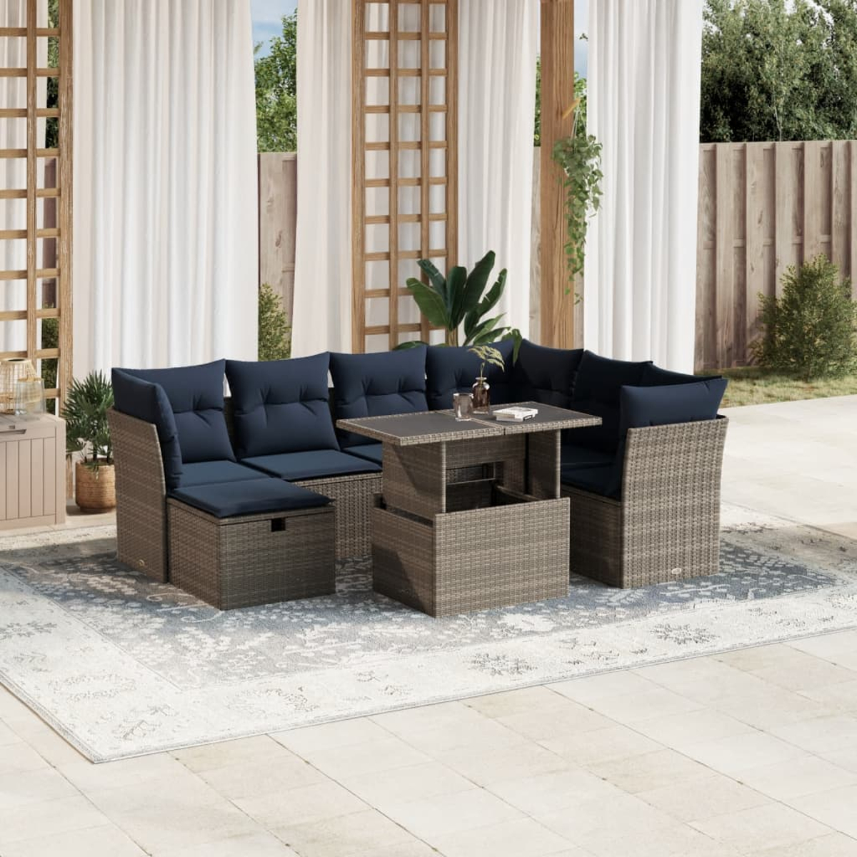 Garten-Sitzgruppe mit marineblauen Kissen. Sie umfasst einen Tisch auf einem gemusterten Teppich. Weiße Vorhänge und Holzrahmen sind im Hintergrund.