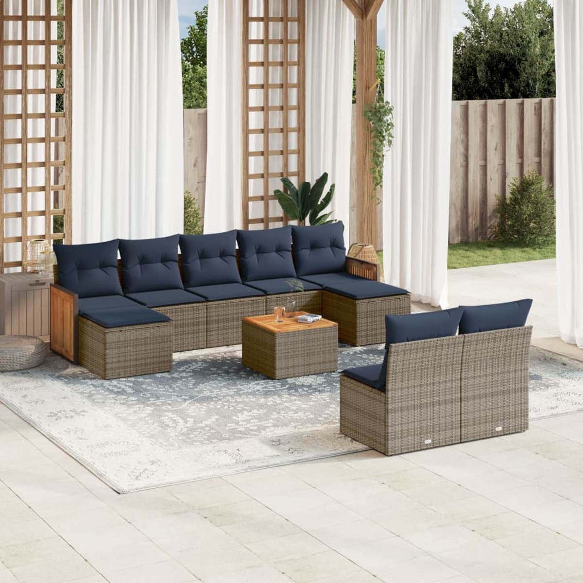 Garten-Sitzgruppe mit blauen Kissen, einem kleinen Tisch und einem Teppich auf der Terrasse. Weiße Vorhänge und Grün im Hintergrund.