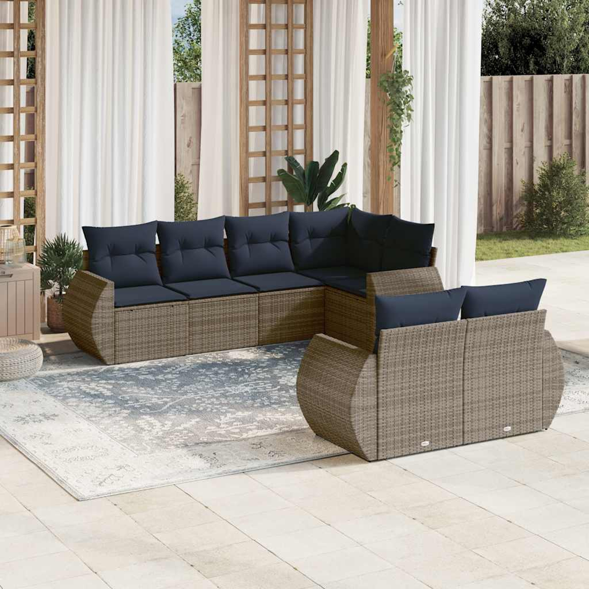Garten-Terrassenset mit braunem Korbmöbelsofa und marineblauen Kissen. Ein Teppich liegt auf der Terrasse. Weiße Vorhänge und eine Holzstruktur sind im Hintergrund.