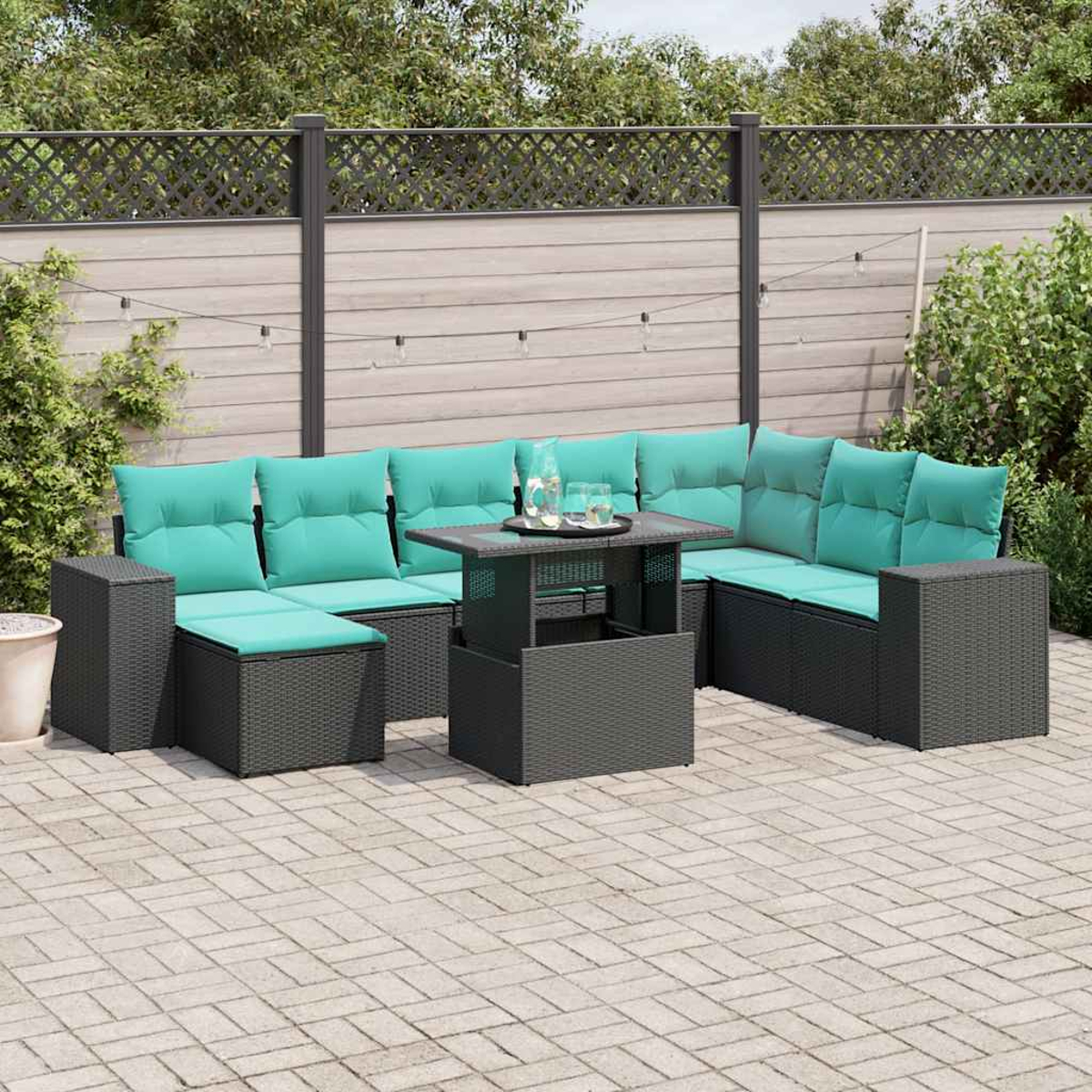 Garten-Sitzgruppe mit türkisfarbenen Kissen und einem Tisch auf einer gepflasterten Terrasse. Im Hintergrund ein Zaun und Grün.