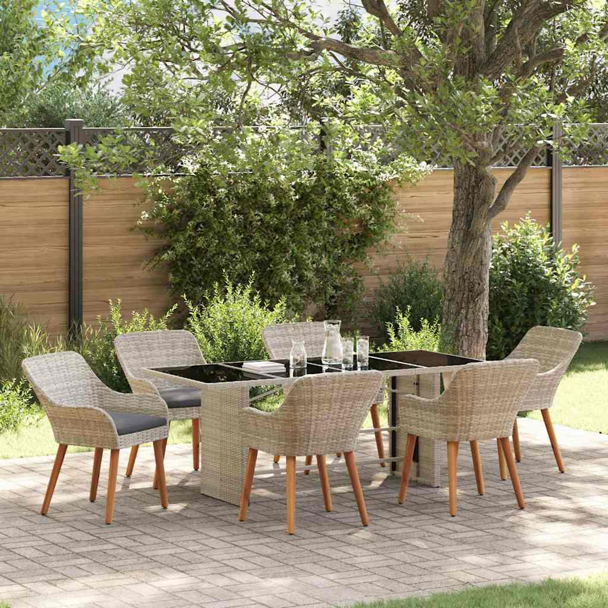 Essgruppe im Freien auf einer Terrasse. Korbstühle umgeben einen Tisch mit Gläsern und einem Krug. Im Hintergrund ein Holzzaun und Bäume.