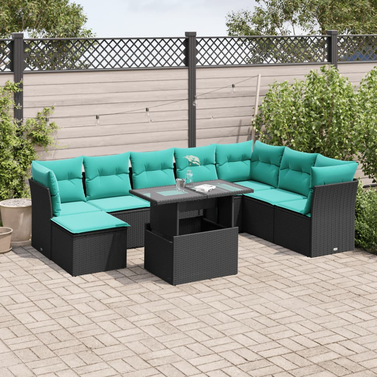 Outdoor-Ecksofa mit türkisfarbenen Kissen auf einer gepflasterten Terrasse. Davor steht ein schwarzer Tisch. Zaun und Pflanzen im Hintergrund.