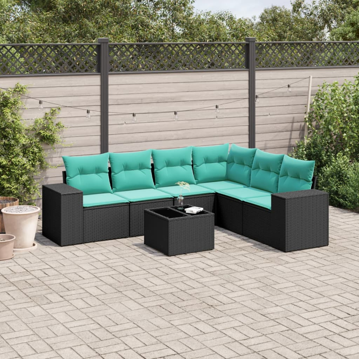 Outdoor-Ecksofa mit türkisfarbenen Kissen und einem schwarzen Tisch. Auf einer Ziegelterrasse, mit Zaun und Grün im Hintergrund.