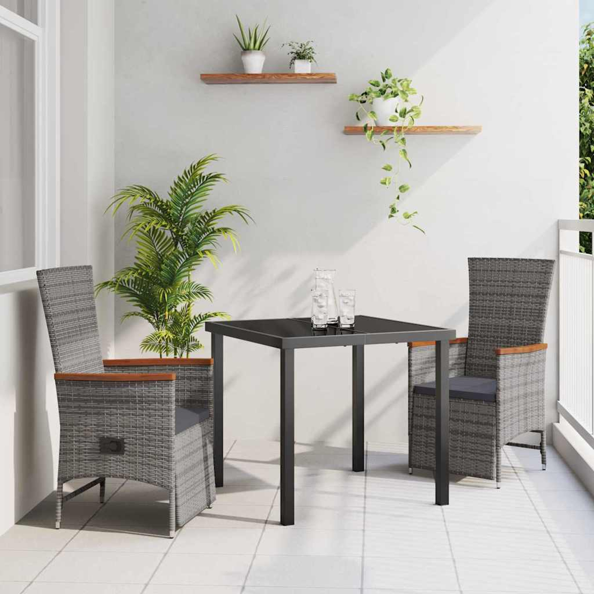 Un set da balcone: due sedie in vimini grigie, un tavolo nero con bicchieri e una pianta alta, con piccole piante su mensole sullo sfondo.