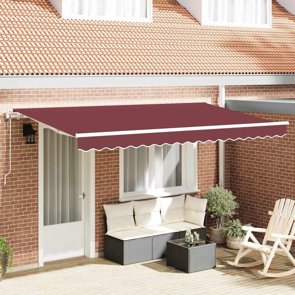 Ein rotes Sonnensegel bedeckt eine Terrassengarnitur mit Sofa, Tisch und Schaukelstuhl. Ziegelmauer und Ziegeldach im Hintergrund.