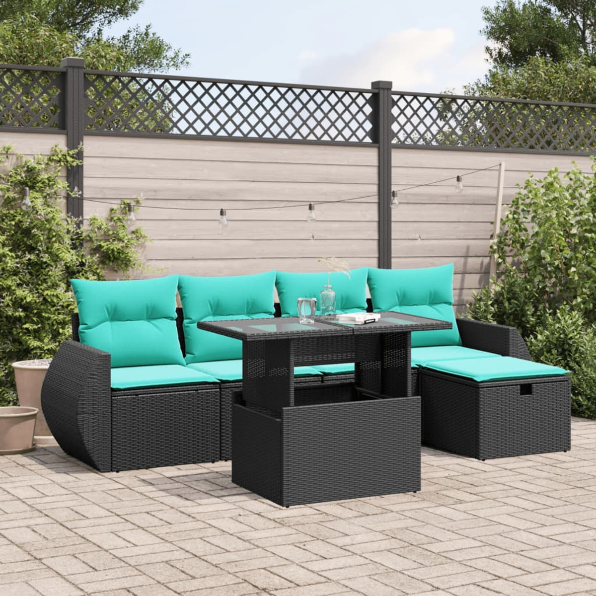 Garten-Set mit schwarzen Korbmöbeln, türkisfarbenen Kissen und einem Tisch mit Glasplatte. Im Hintergrund ein Zaun und Grün.