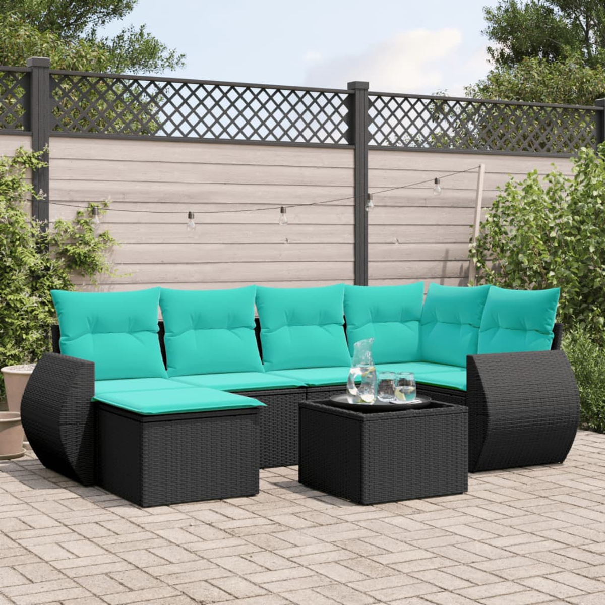 Schwarzes Outdoor-Wicker-Sofa mit türkisfarbenen Kissen und einem Couchtisch auf einer Ziegelterrasse. Im Hintergrund ein Holzzaun.