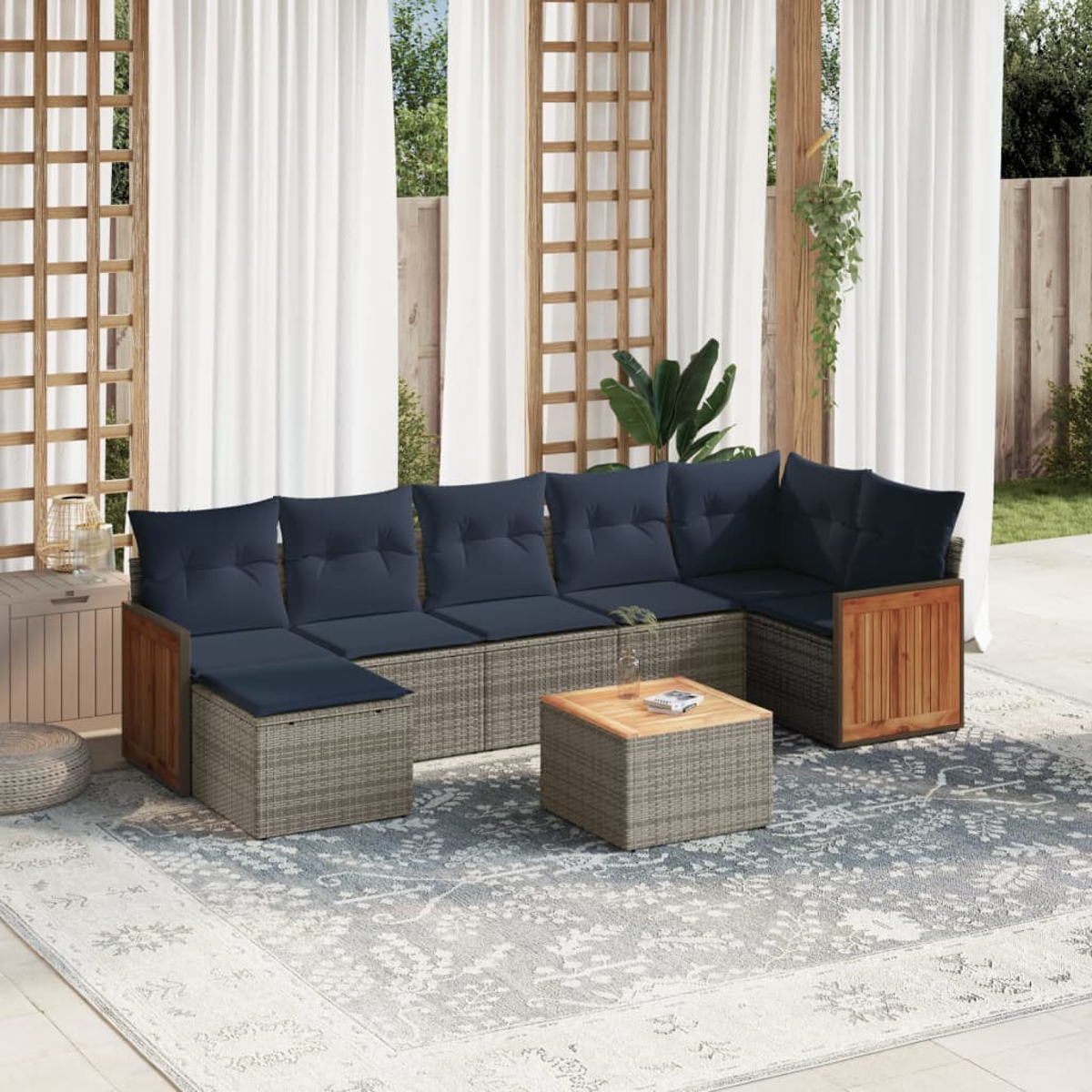 Un sofá seccional exterior con cojines azules, una mesa de café de madera y una alfombra estampada frente a cortinas blancas.
